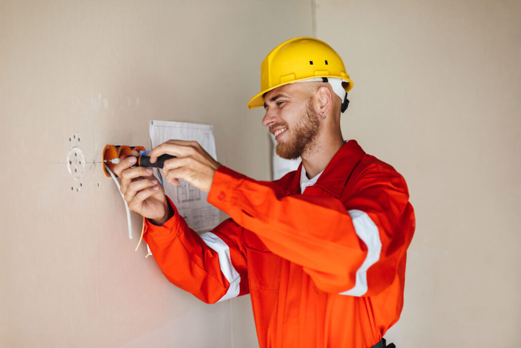 Smiling foreman in orange work clothes and yellow hardhat using